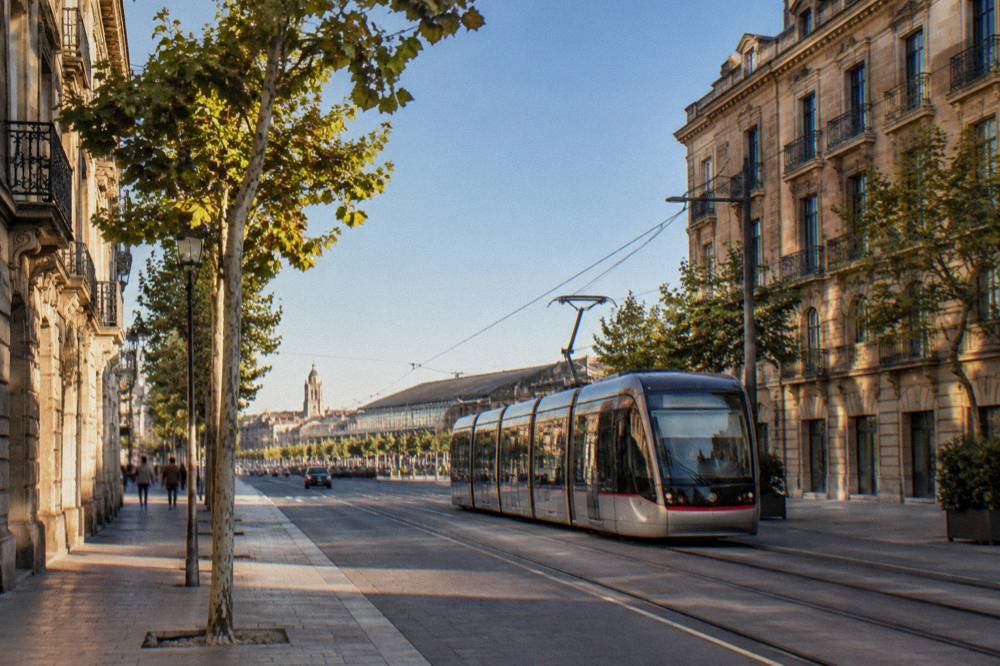 A modern tram moving along a city street with historic stone buildings on both sides