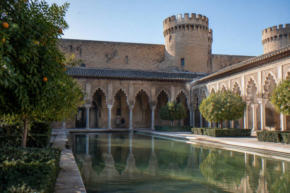 A sunlit Moorish palace courtyard with carved arches and a reflecting pool