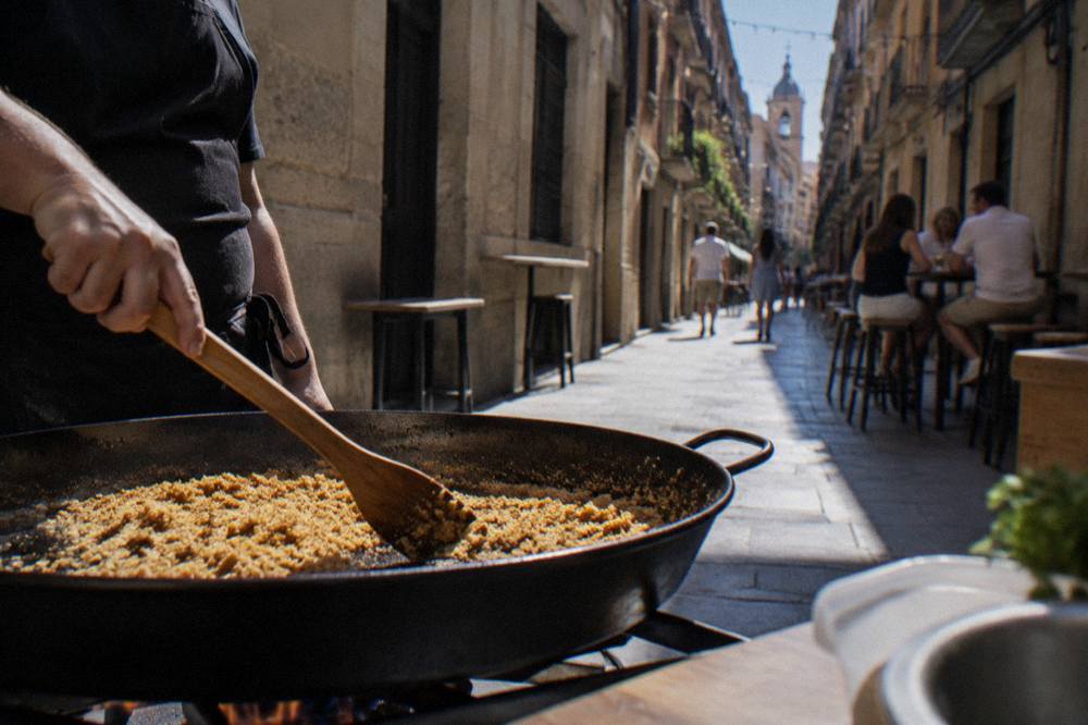 A cook stirring a wide pan of breadcrumbs with a wooden spatula over moderate heat