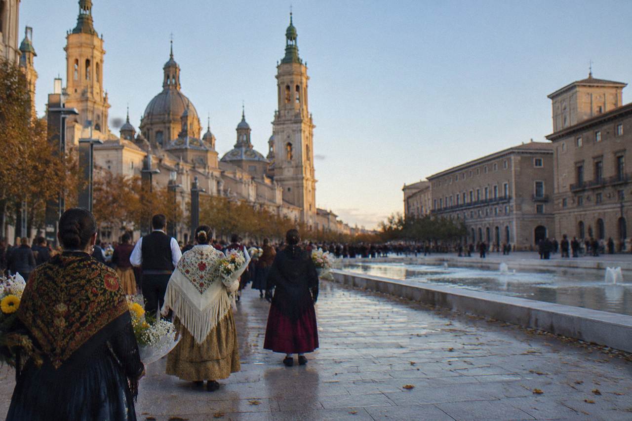 Crowds in traditional Aragonese dress carrying flower bouquets along a wide city avenue toward a basilica