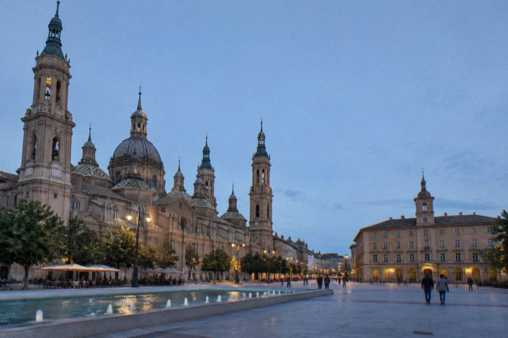 A narrow old-town street of stone buildings with bar terraces in the evening in Zaragoza