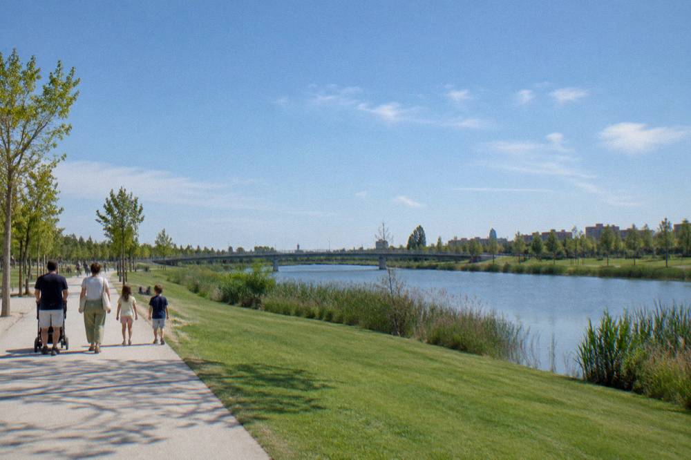 Families walking along a wide riverside path with trees in the Parque del Agua in Zaragoza