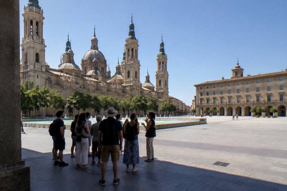 A small guided tour group listening to a guide in a stone square in Zaragoza old town