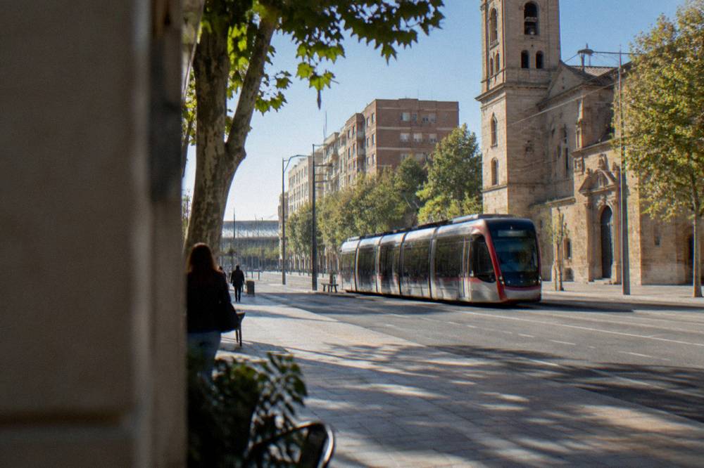 A modern tram passing a stone church facade on a wide city avenue