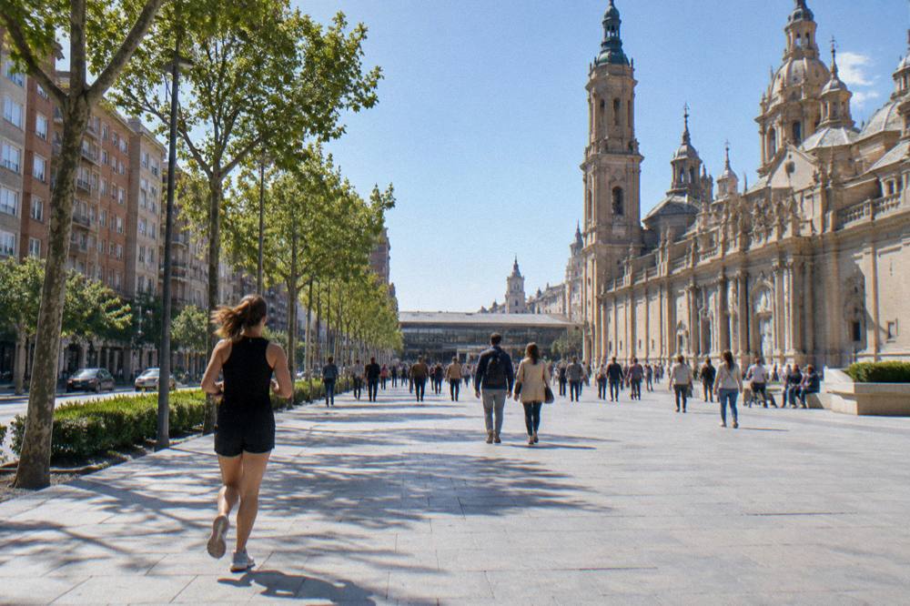 A wide stone plaza with a baroque basilica facade and crowds walking under a bright sky