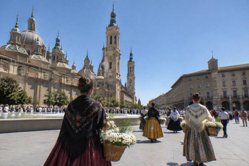 People in traditional Aragonese costume carrying baskets of white flowers through a crowded city street