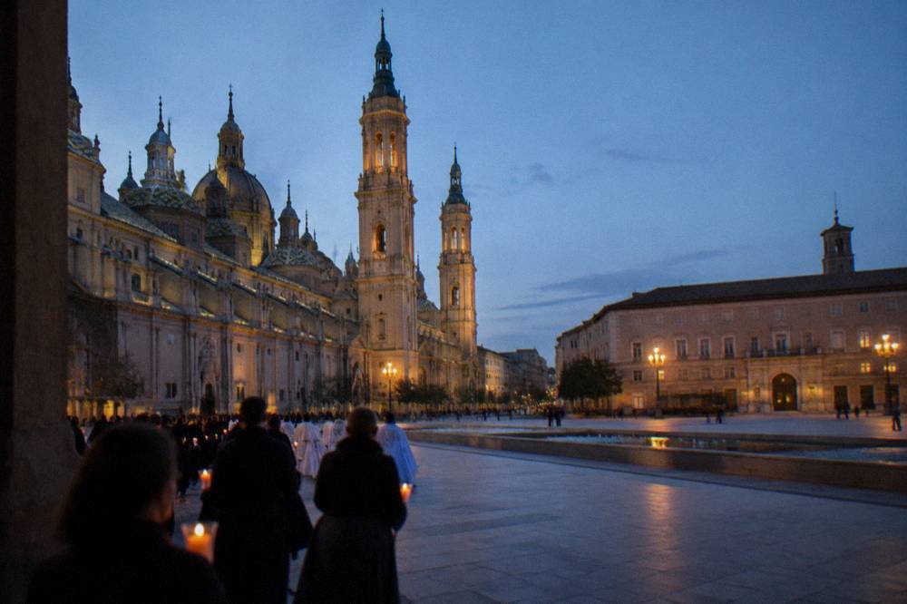 A candlelit procession winding past a Gothic cathedral facade at night
