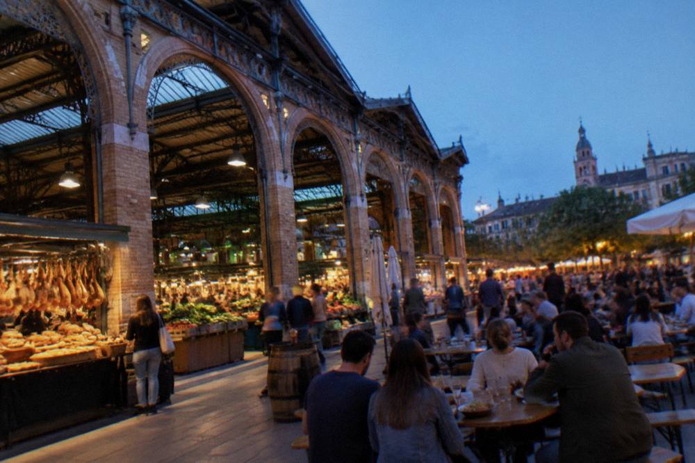 An outdoor festival crowd eating at street tables in a plaza in the evening