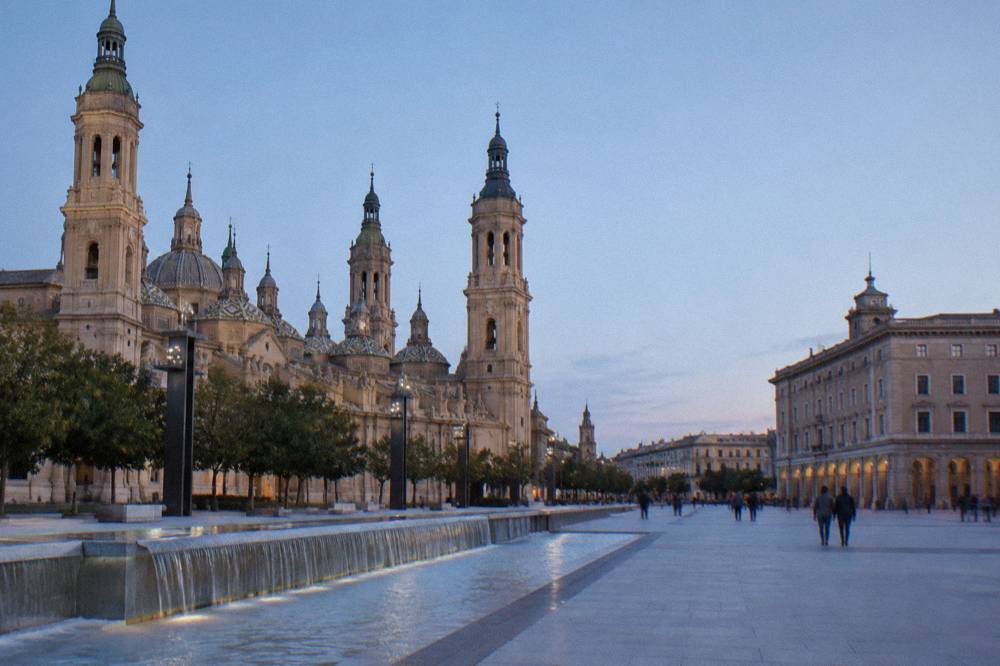 A narrow old-town street in Zaragoza with worn stone walls and a small square beyond
