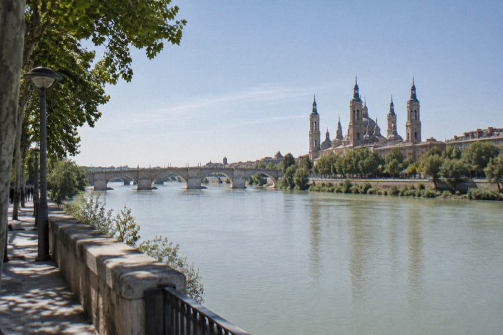 The Ebro river in Zaragoza seen from a bank with the stone bridge in the distance