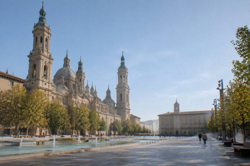 A tree-lined park path in Zaragoza with benches and dappled shade