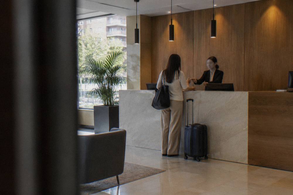 A small suitcase standing beside a hotel reception desk while a receptionist hands over a room key