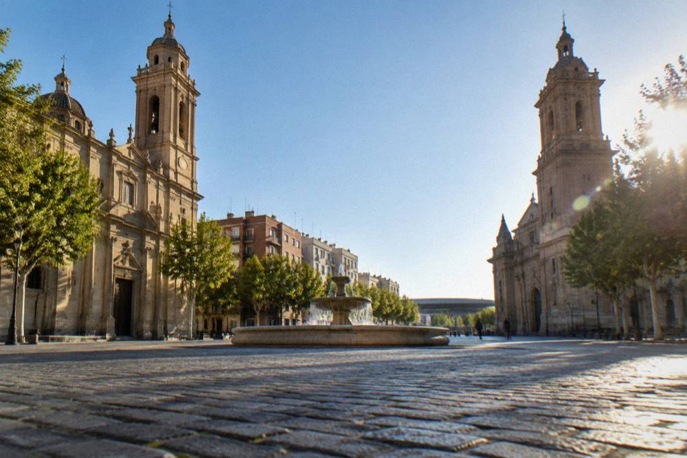 An empty cobbled square between two large historic churches with a fountain in the centre on a clear day