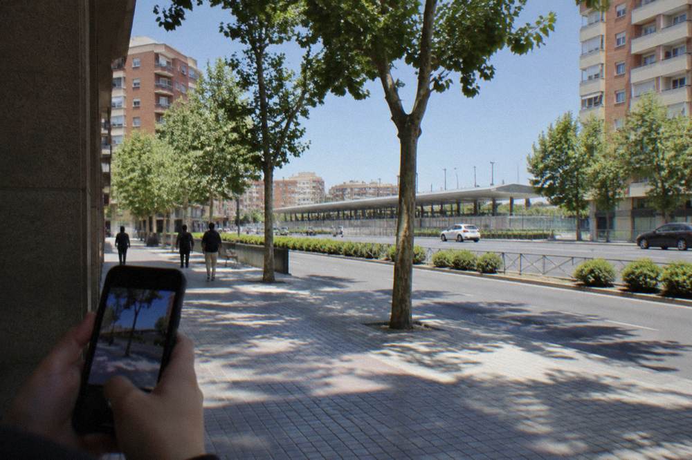 A person holding a smartphone showing a map while standing on a sunlit pedestrian shopping street lined with awnings