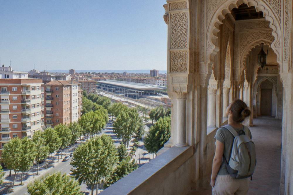 A visitor with a light day pack looking up at an ornate Moorish arched hallway with carved plaster decoration