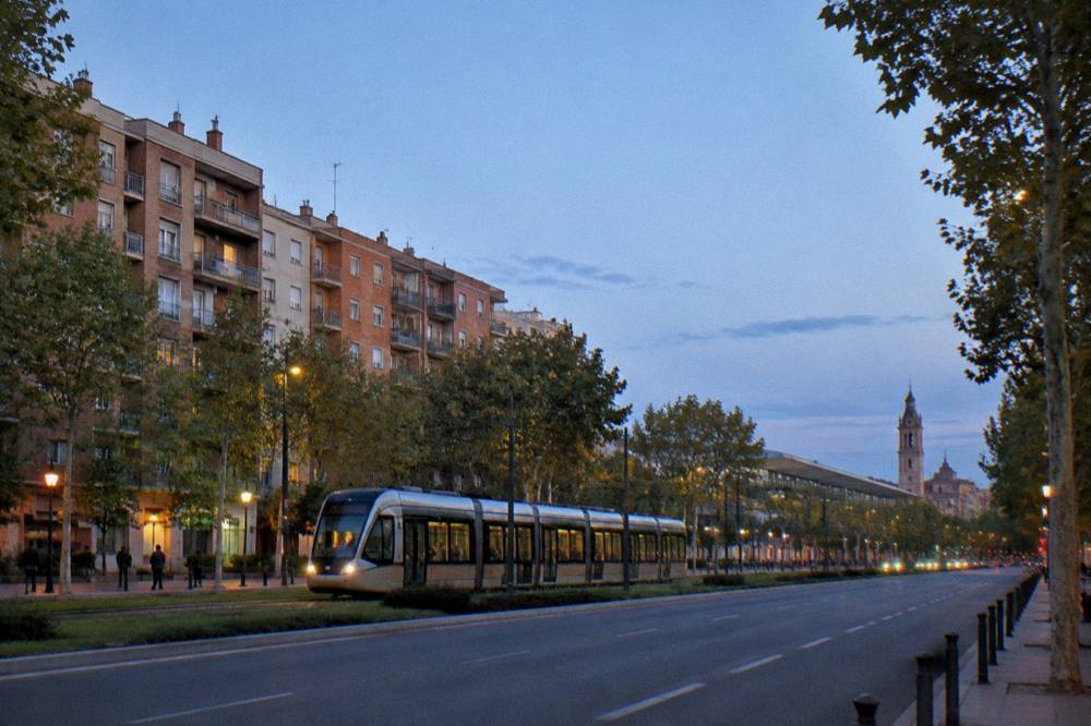 A tram gliding along a tree-lined avenue with apartment balconies and a distant church tower in early evening light