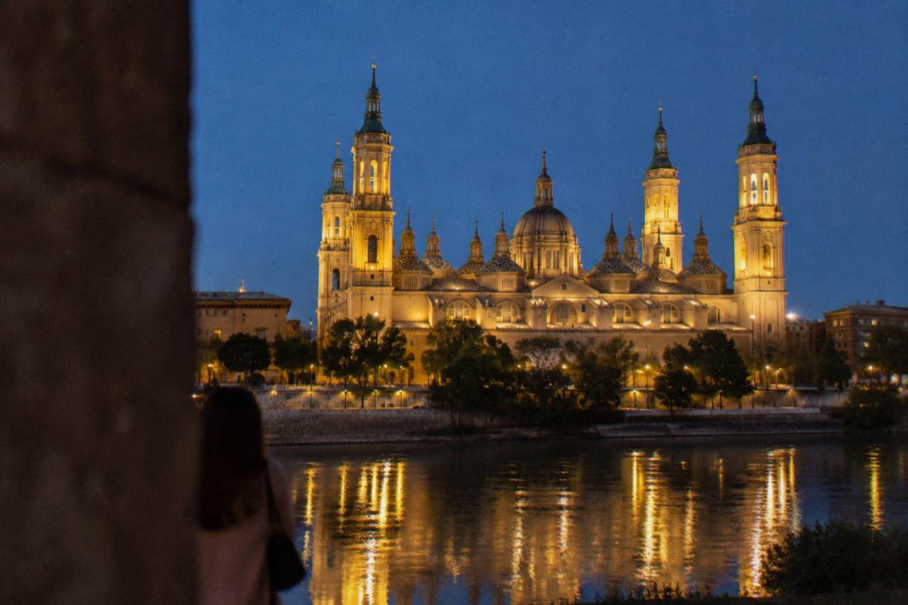 Illuminated Basilica del Pilar and its towers reflected in the Ebro river at dusk