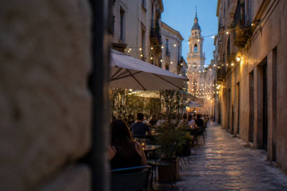 An open-air terrace with people at tables under string lights on a warm evening