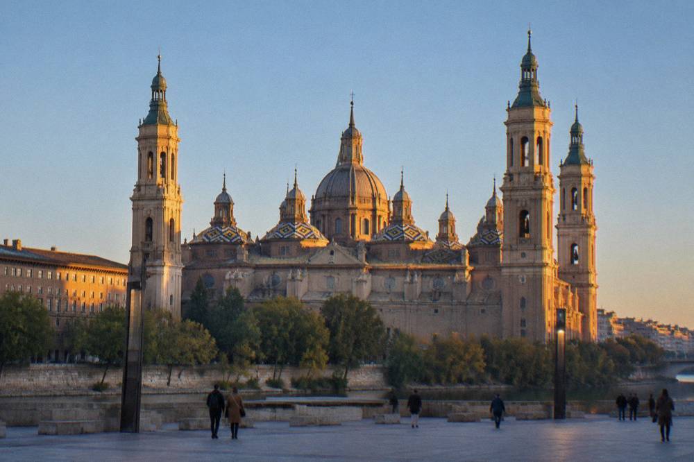Low evening sunlight striking the domes of the Basílica del Pilar from the Ebro riverbank