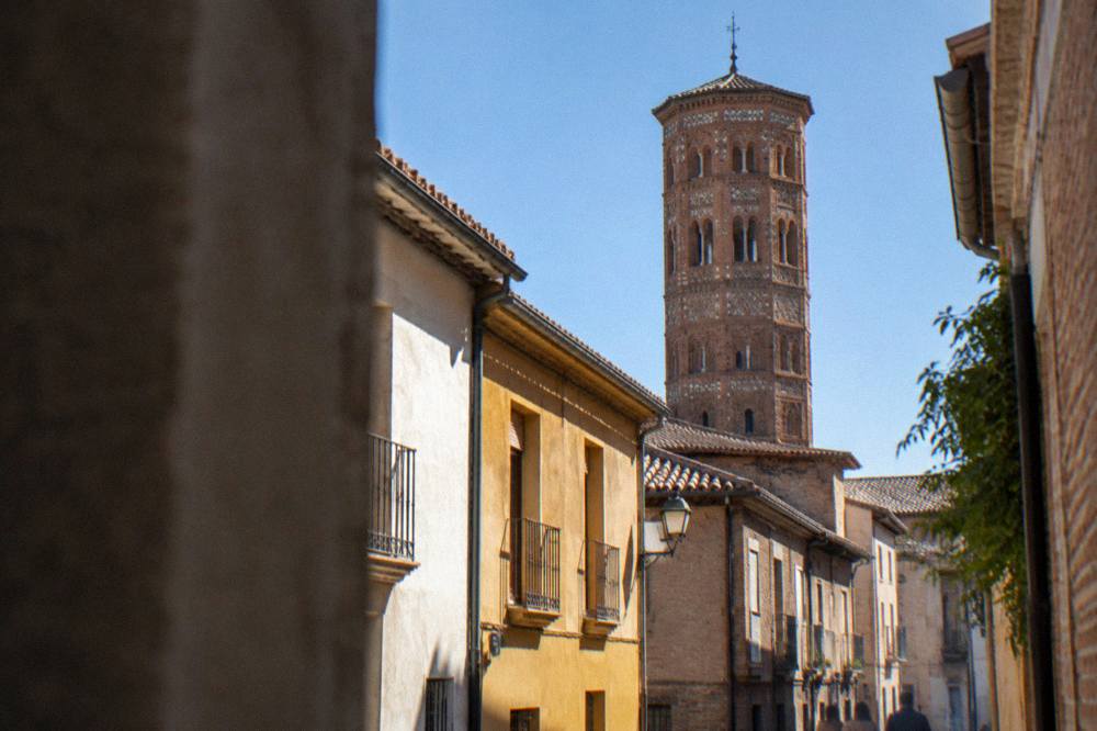 A quiet narrow street in the San Pablo barrio with the Mudéjar brick tower rising above the rooftops