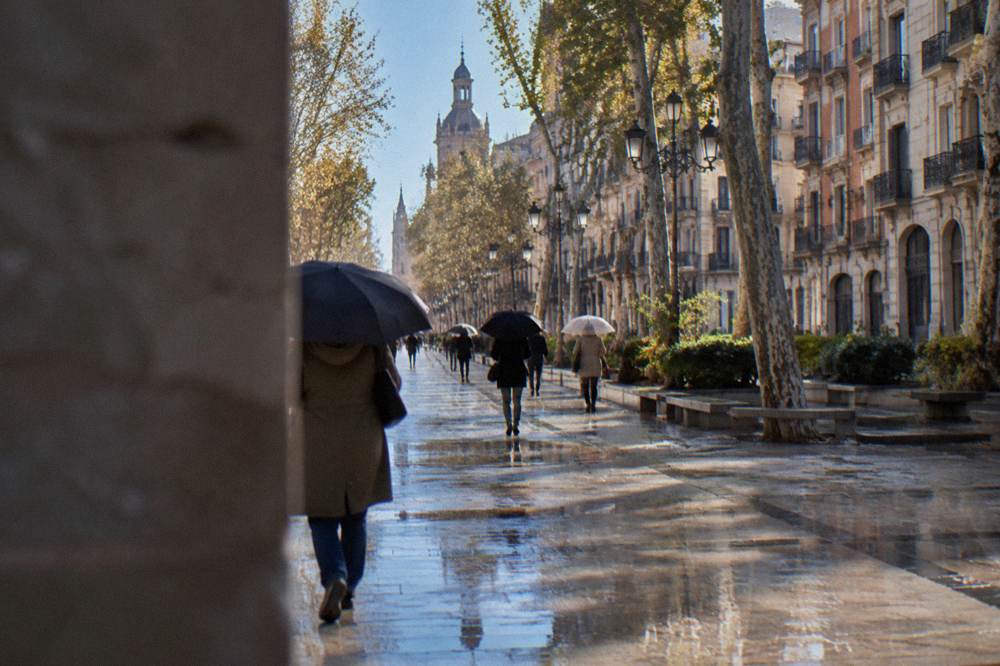 People walking with umbrellas along a wet street in central Zaragoza near the Paseo de la Independencia
