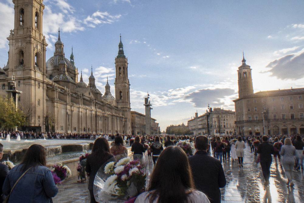 A dense crowd filling a street in Zaragoza during a festival with people carrying flower bouquets