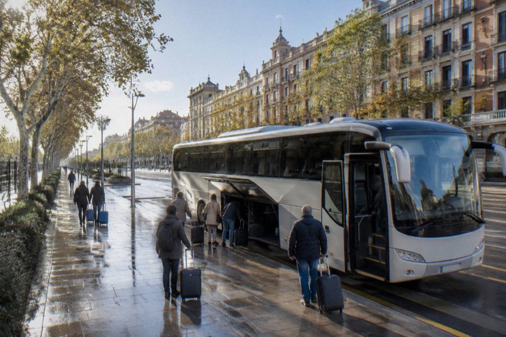 A bus waiting at an airport terminal curb with passengers loading luggage