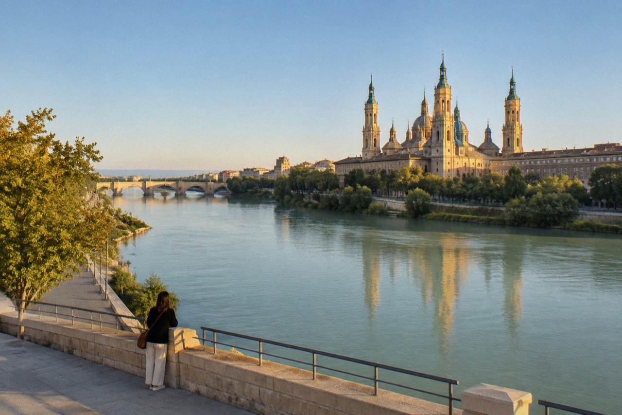 A lone traveller looking across the Ebro river toward the Basílica del Pilar at golden hour