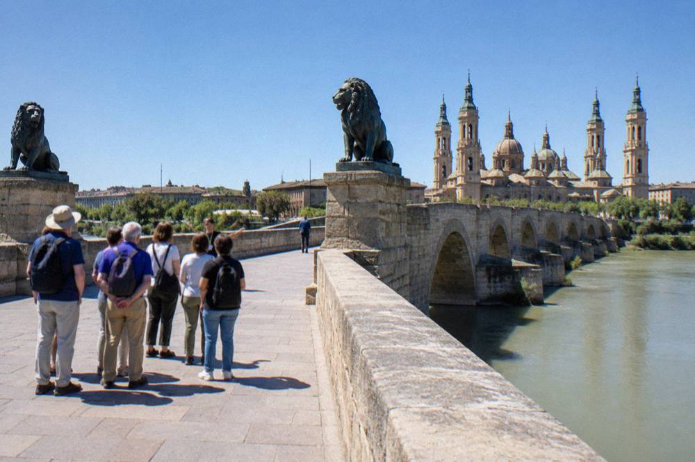 A small walking tour group gathered around a guide near the Puente de Piedra in Zaragoza