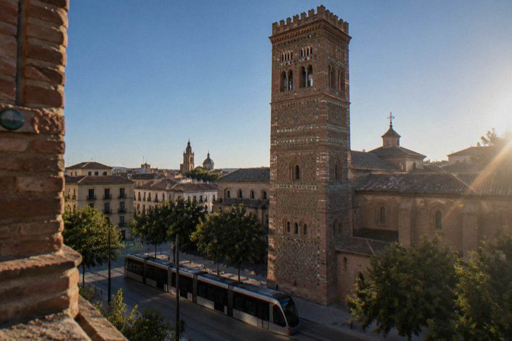 A modern tram passing a Mudéjar brick church tower on a street in Zaragoza