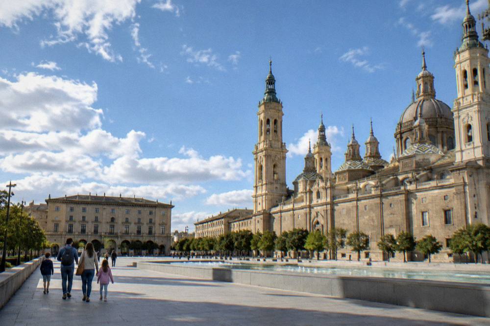 A family with two children walking along a riverside path in Zaragoza with the stone bridge in the background