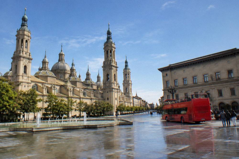 Open-top sightseeing bus parked beside a historic square in Zaragoza