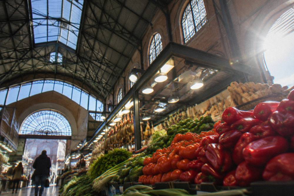 A market stall piled with red peppers, tomatoes and green vegetables under bright lights