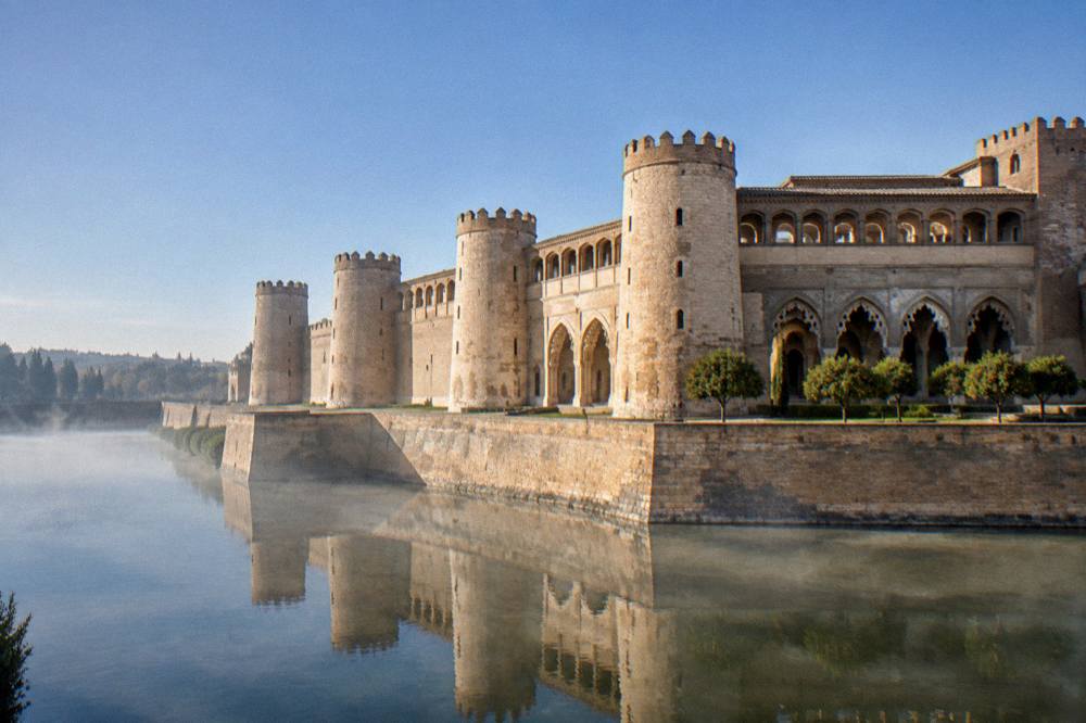 The Aljafería palace in Zaragoza seen from its moat with Islamic arches reflected in the water