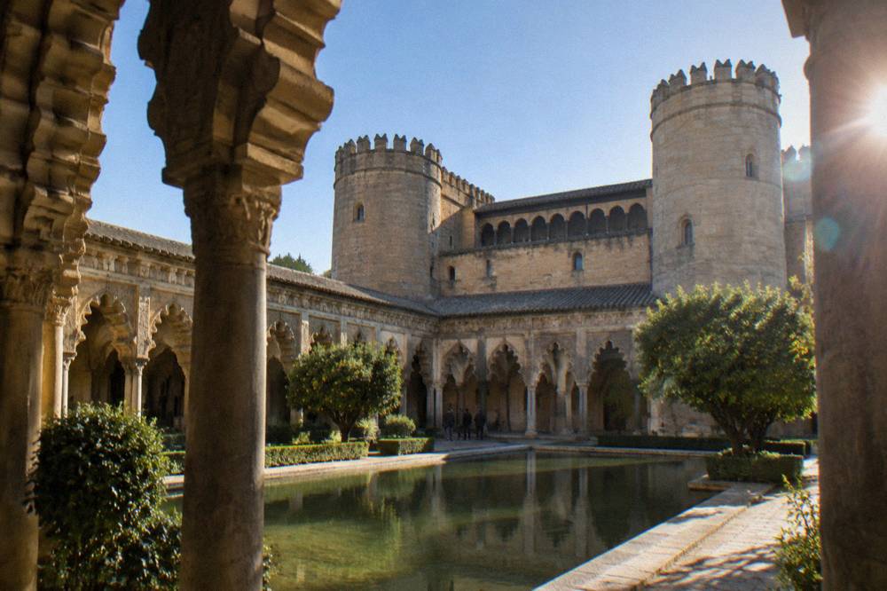 The ornate arched courtyard of the Aljafería palace under a clear sky