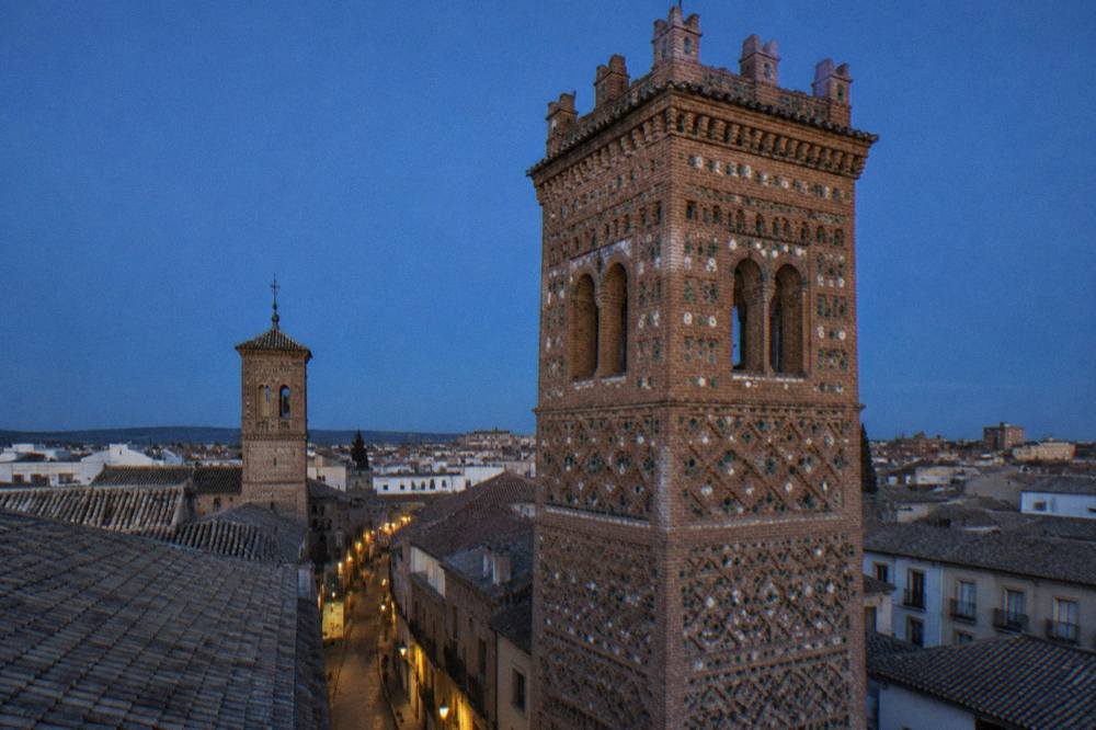 A quiet old town street with brick Mudejar towers against a blue sky