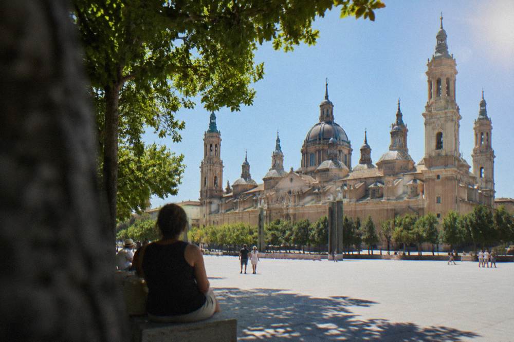 A hot July afternoon with shade seekers resting under trees beside the Basílica del Pilar