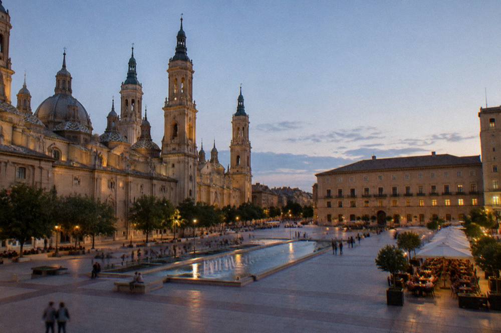 Evening diners at outdoor tables in a lit old town square in Zaragoza
