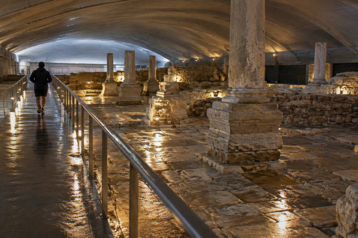 Excavated Roman paving and column bases lit under a museum roof