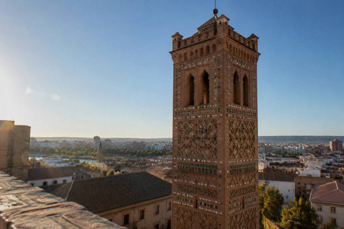 A tall Mudejar brick tower with geometric patterned panels against the sky