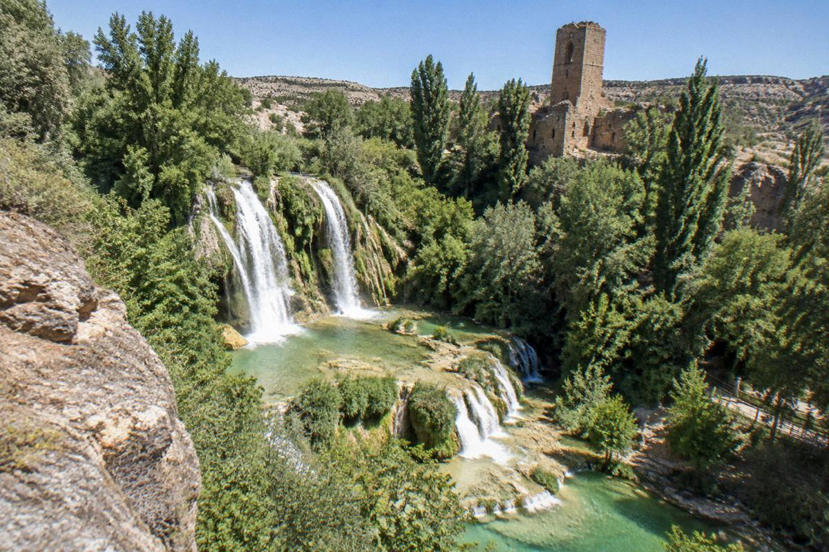 A waterfall dropping through green gardens beside an old monastery wall