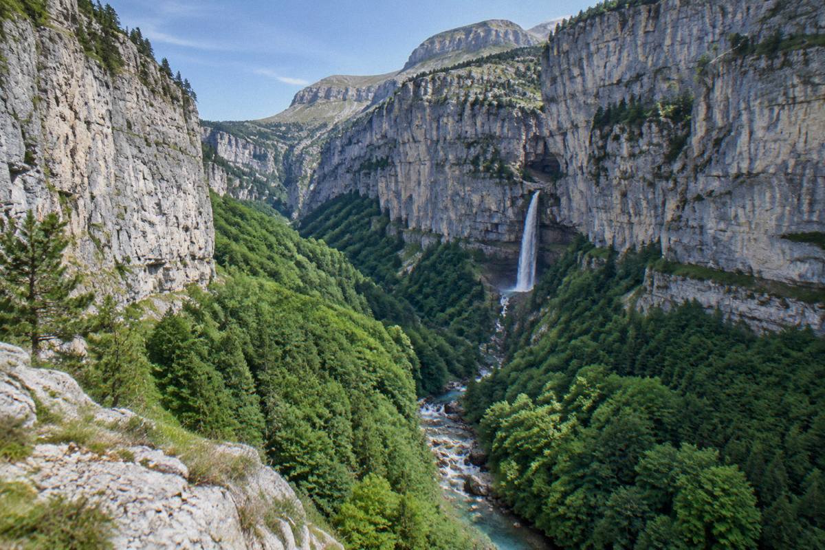 A green glacial valley with a waterfall and limestone cliffs above