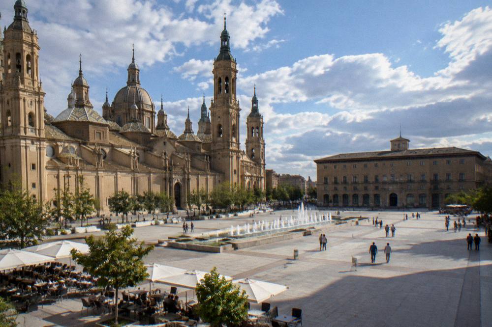 A wide pedestrian square in Zaragoza old town with café tables in sunlight