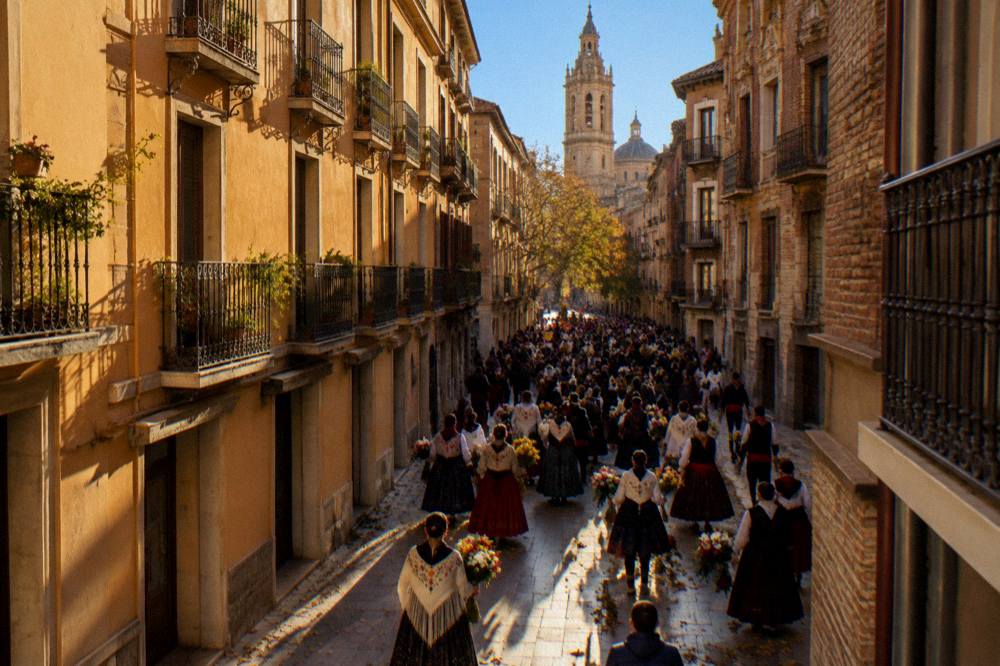 Crowds in regional Aragonese dress filling a city street during the Fiestas del Pilar flower offering