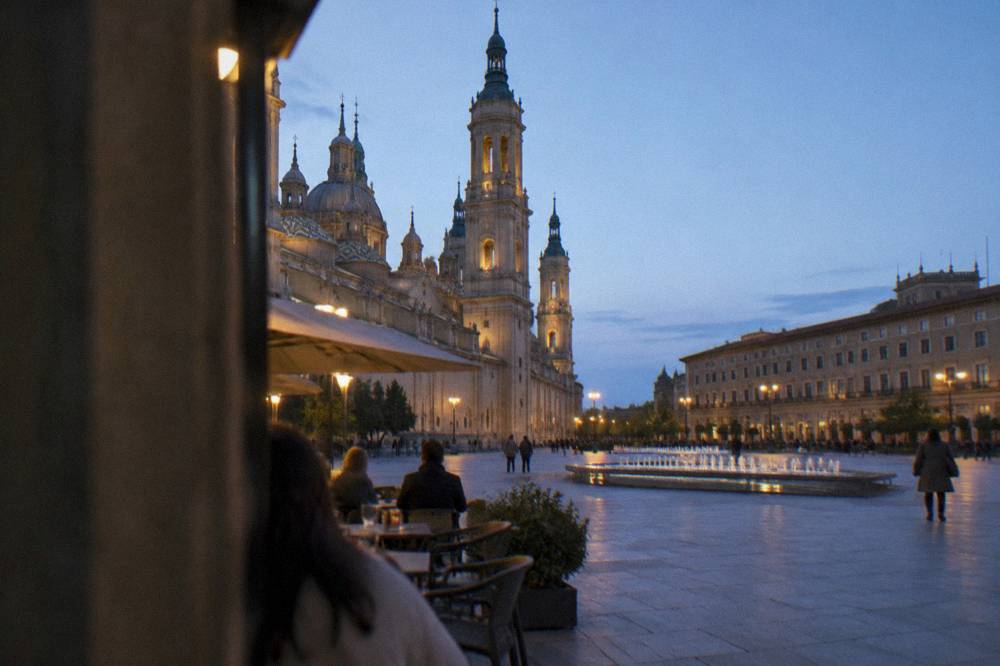 A narrow lamplit street in the old town of Zaragoza with bar terraces in the evening