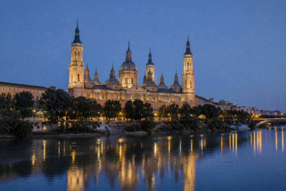 The illuminated Basilica del Pilar reflected in the Ebro river at night