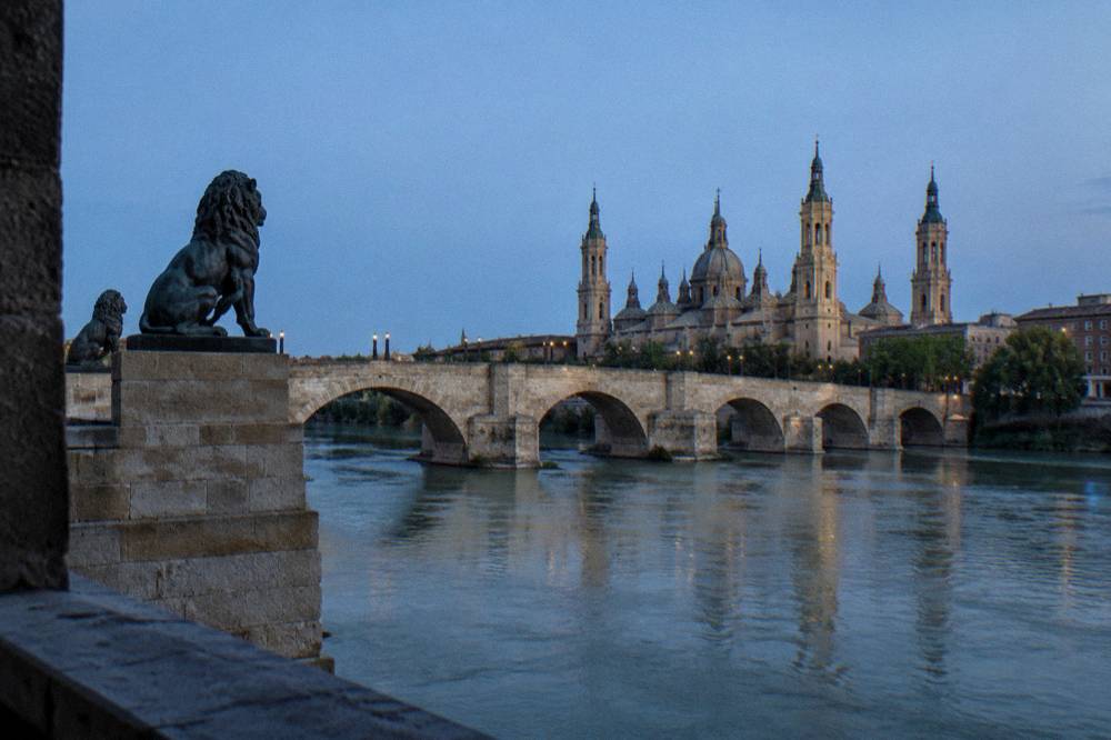 The stone arches of the Puente de Piedra bridge over the Ebro with bronze lion sculptures