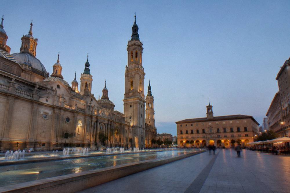 A narrow old town street in Zaragoza lined with small bars and outdoor tables in the evening