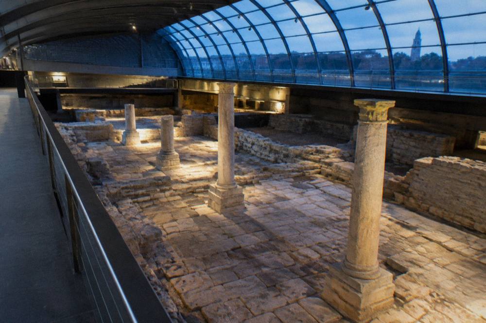 Interior of the Roman forum museum in Zaragoza with excavated stone remains under a glass roof