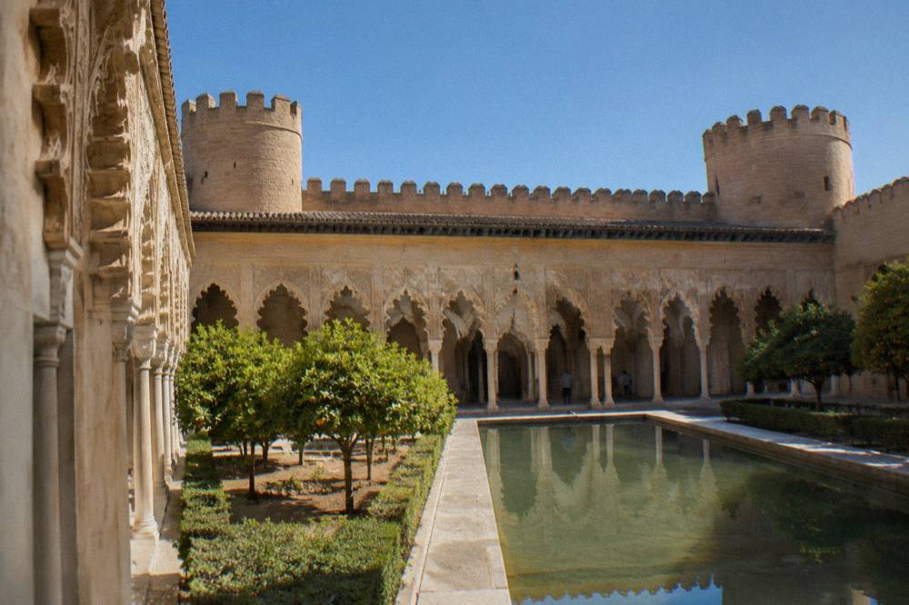 The ornate plaster arches of the Aljafería palace courtyard in soft morning light